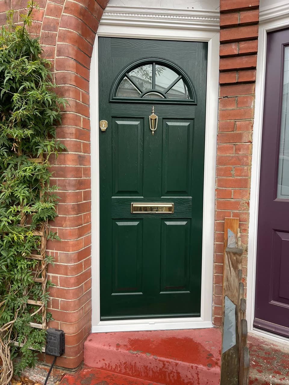 Dark green front door with an arched glazed top in a brick porch
